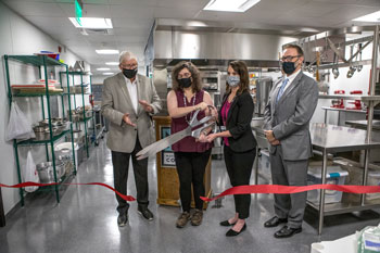 Red ribbon being cut by oversized scissors in a grand reopening of the hospitality center at NPC. 