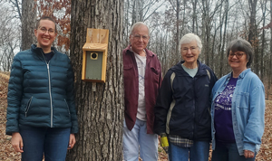 Tree with bird box attached and people standing around the tree.